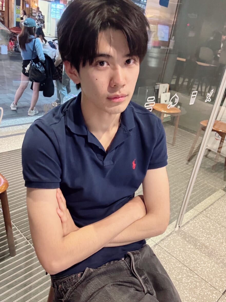 腕を組んでカフェの椅子に座る、旅行中の稲井孝太朗