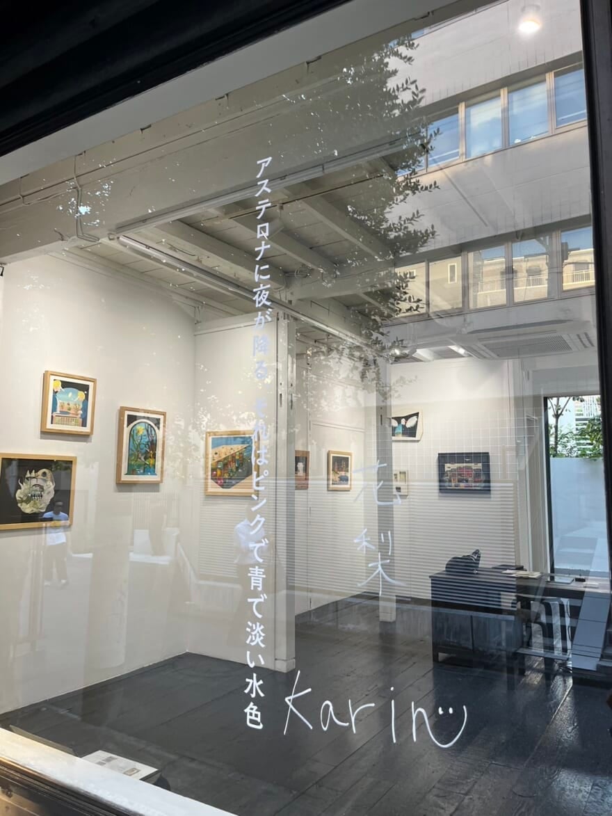 個展会場の窓。個展のタイトルである「アステロナに夜が降る、それはピンクで青で淡い水色。」と書かれている。