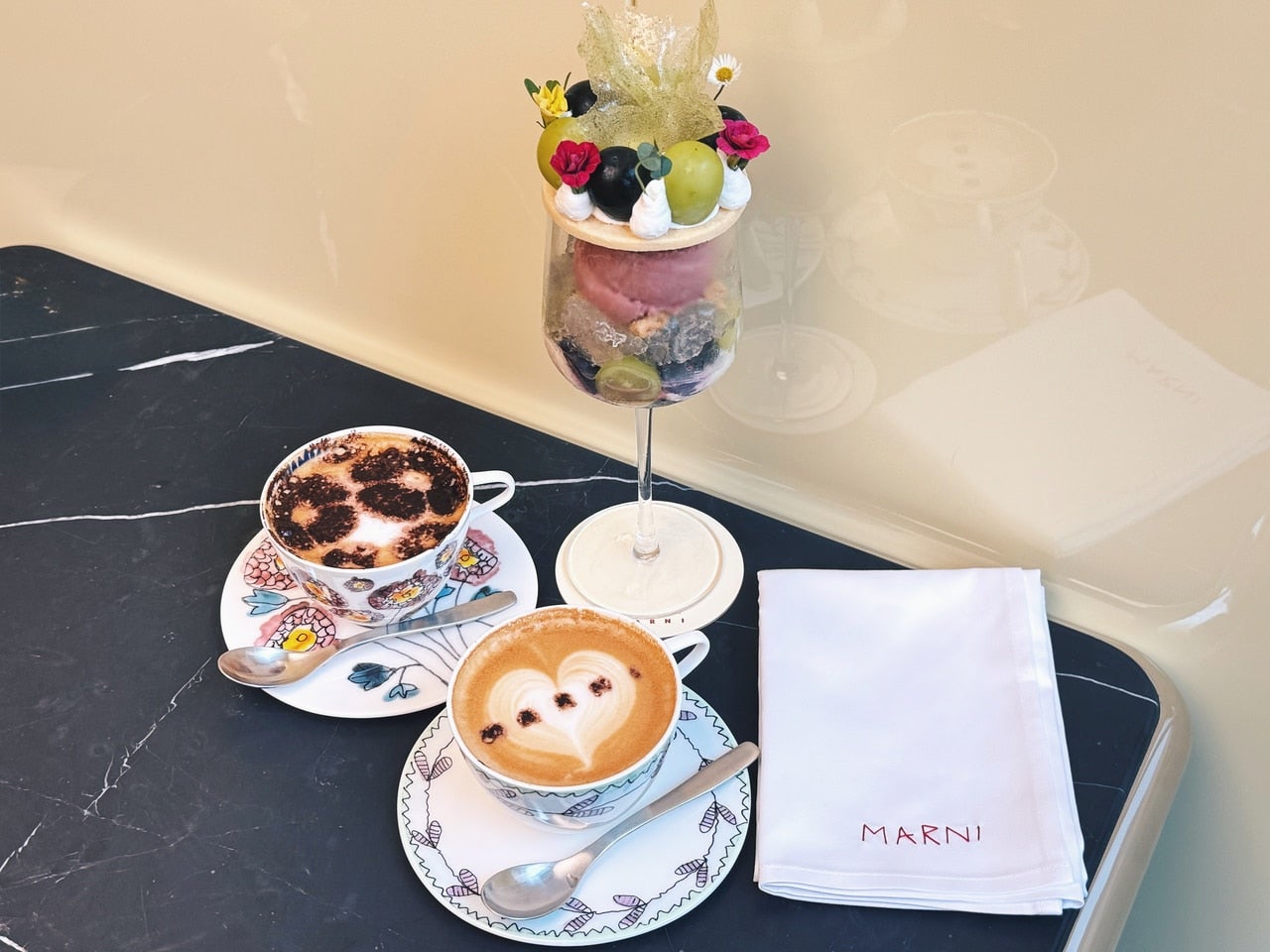 銀座「マルニ カフェ」シグネチャーメニューのロゴ入りカプチーノとパフェ