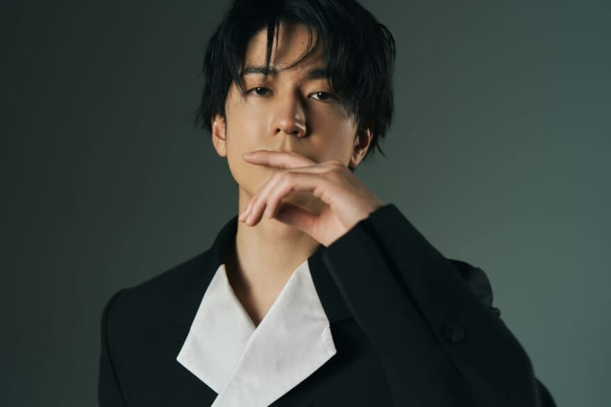 中島裕翔さんのメンズノンノ限定公開ショット。黒い背景の前で、口元に手を置いた中島裕翔さんが立っている。