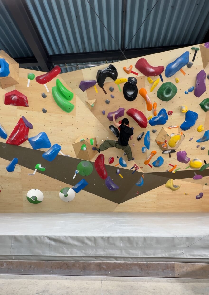 ボルダリングを楽しむメンズノンノモデル鈴木仁。壁に取り付けられたホールドをつかんでいる、後ろ姿が映っている。