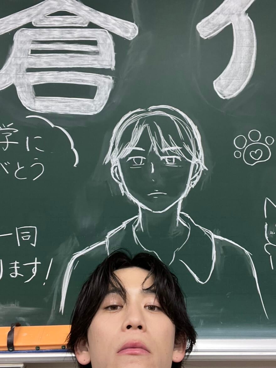自分の似顔絵が描かれた黒板の前で写真を撮るメンズノンノモデル小方蒼介