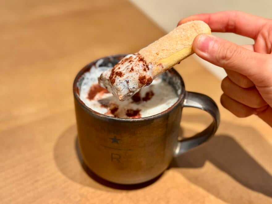 スタバ中目黒「ロースタリー東京」2025クリスマス。ホリデーメニュー1階 メインバー『バレルエイジド ティラミス ラテ』ビスコッティにディップしている様子