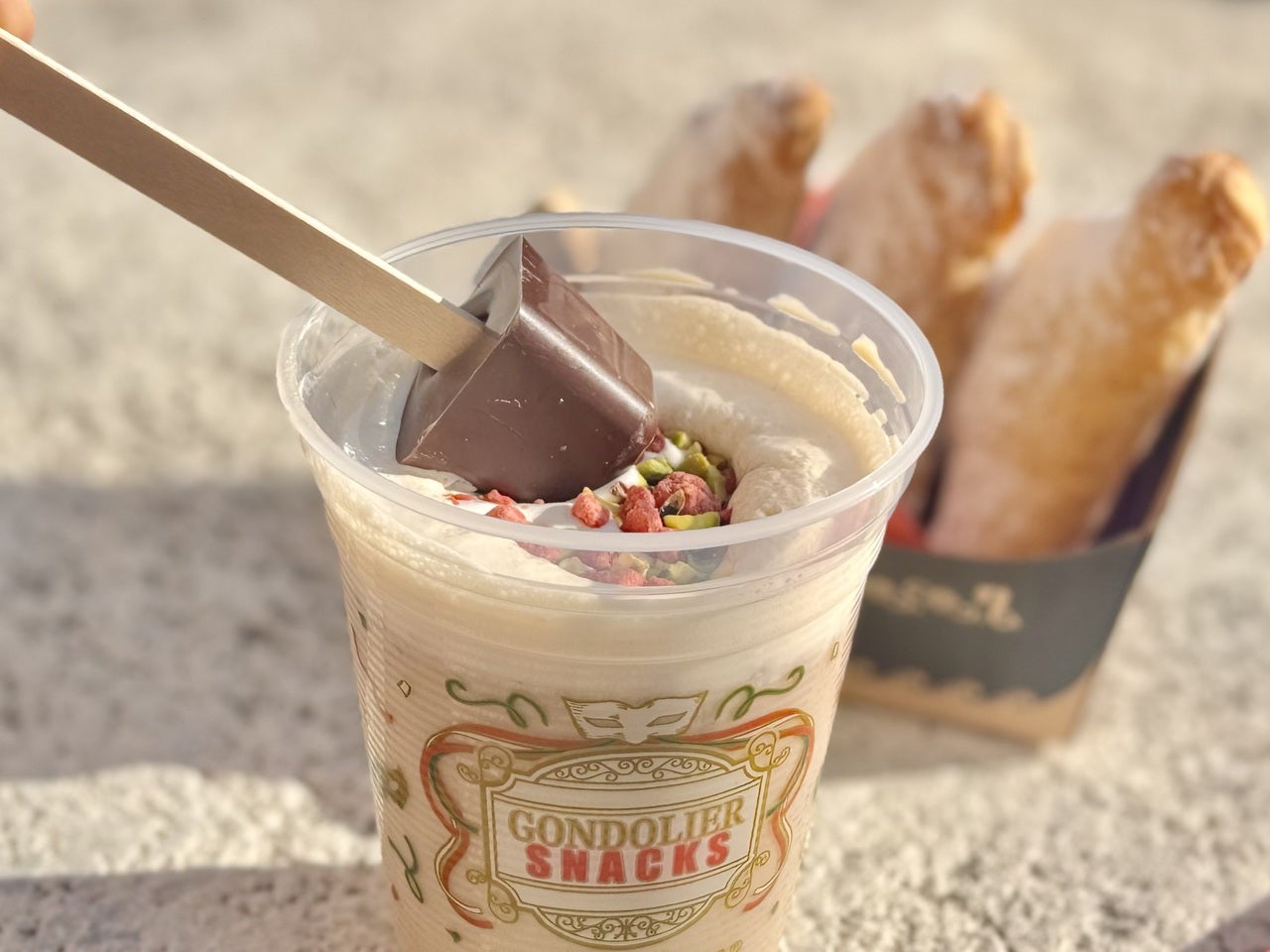 ディズニーシー食べ歩き限定「ピスタチオとストロベリーのカフェモカ」にチョコスティックをディップしている様子