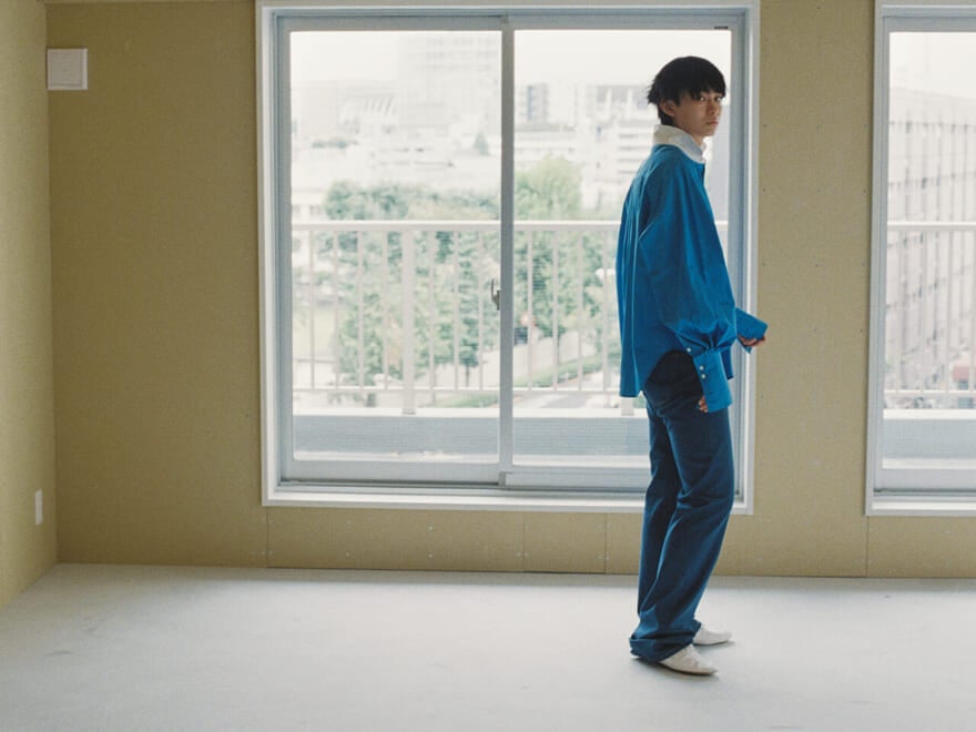 セリーヌの2025年秋冬新作から、ブルーのクレリックシャツを着用する豊田裕大さん