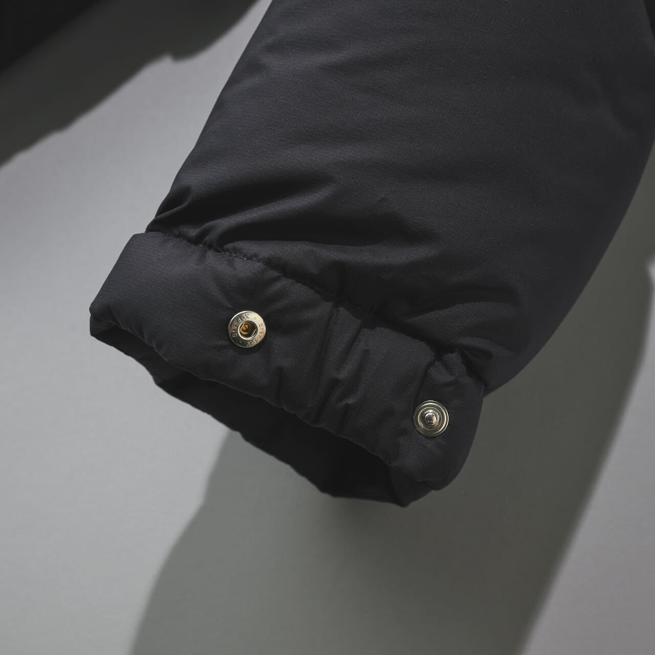 オーラリーの新作黒ダウン/SUPER LIGHT NYLON RIPSTOP DOWN BLOUSONの袖スナップボタン