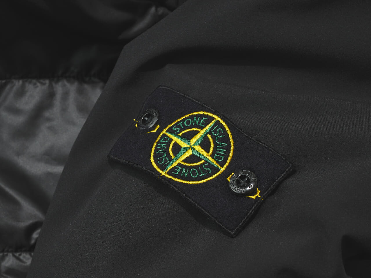ストーンアイランドの黒い中綿ジャケットの袖ロゴ寄り