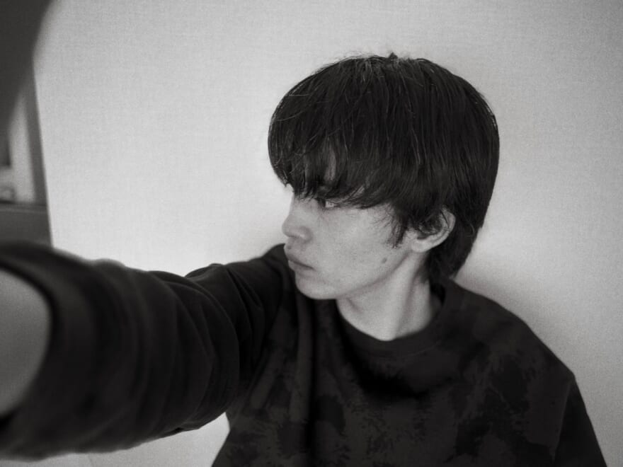 モノクロ写真の中田圭祐。黒いスウェットを着ている。手を前に伸ばしている