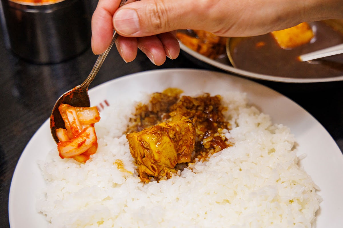 卓上の玉ねぎアチャールをミステリアスなカシミールカレーにかけている様子
