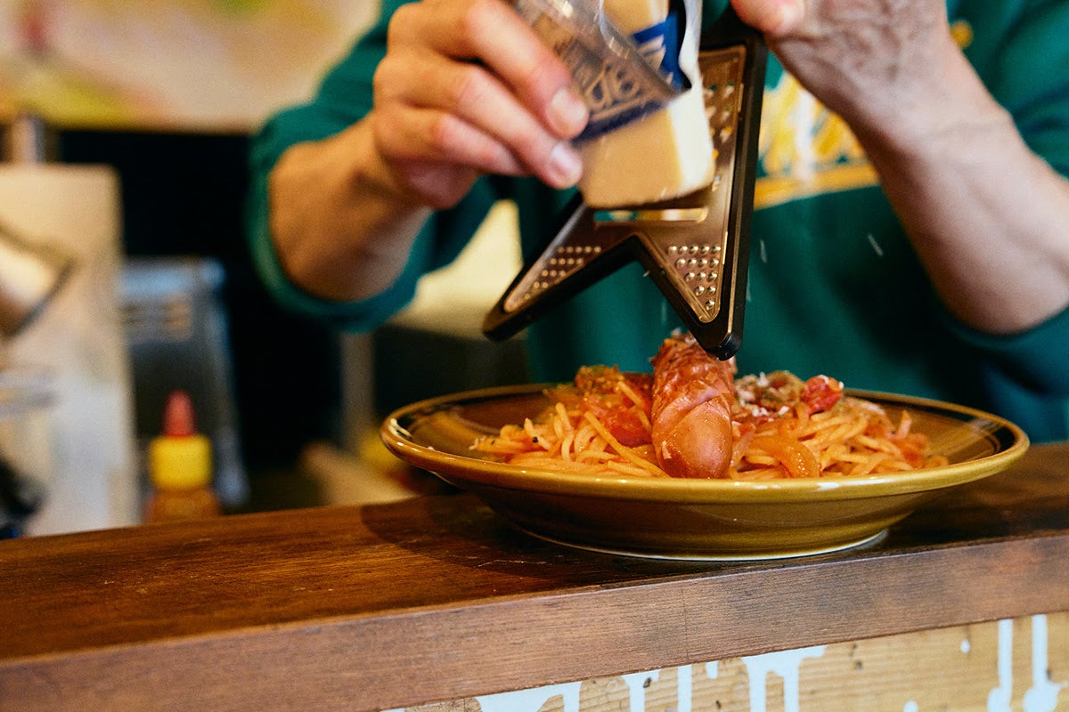 「高円寺メタルめし」ギターの形をしたチーズシュレッダーでパスタにチーズを削っているヤスさん1