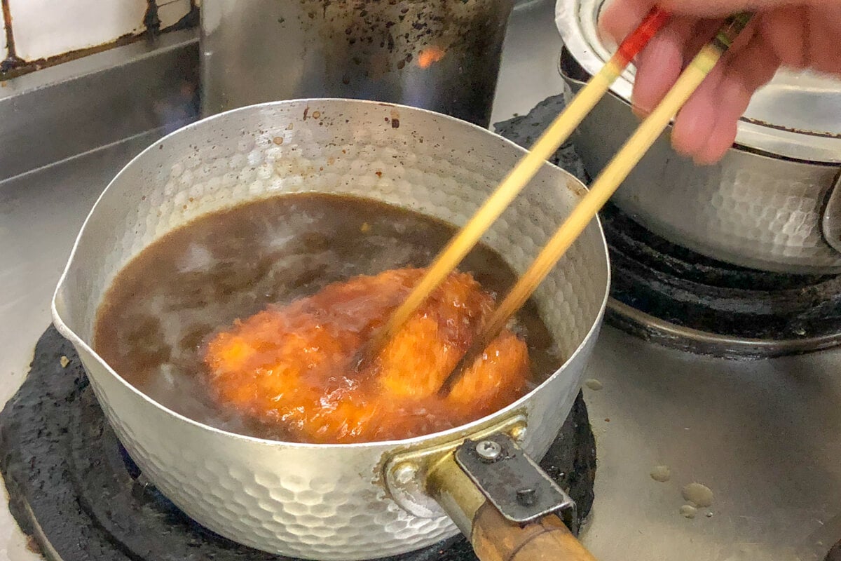 愛知県名古屋市『玉屋』分厚いとんかつが鰹出汁の効いた煮汁に浸されている様子