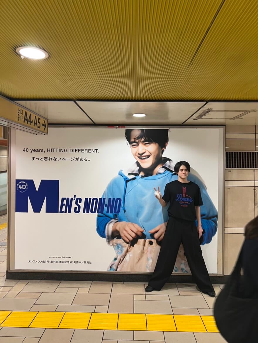 駅の中の広告の前でピースをする鈴鹿。広告には大きく鈴鹿自身が写っている。