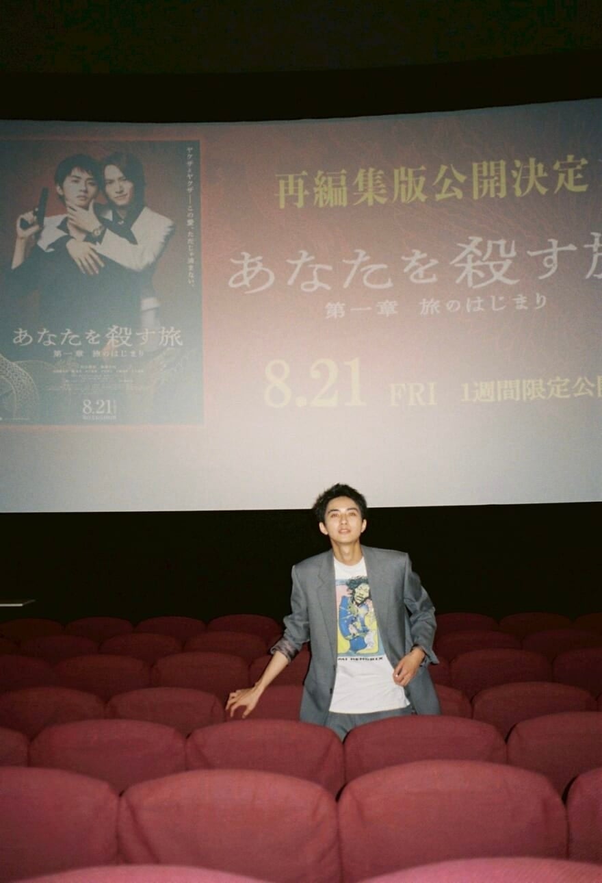 映画館に立つ髙橋大翔。後ろのスクリーンに『あなたを殺す旅』の画像が写っている