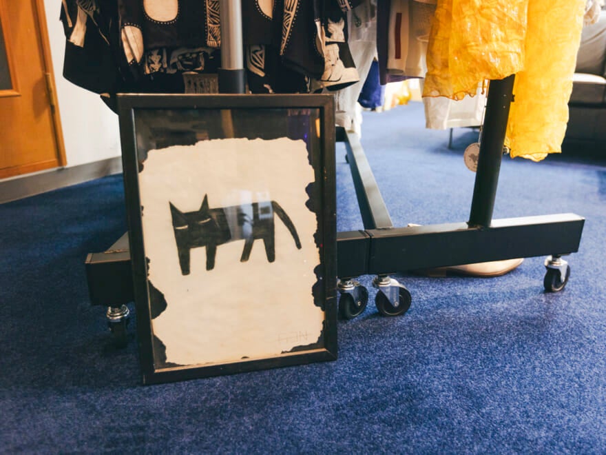 ラックの足元に置かれた作品。黒猫のようなイラストが額装されている。