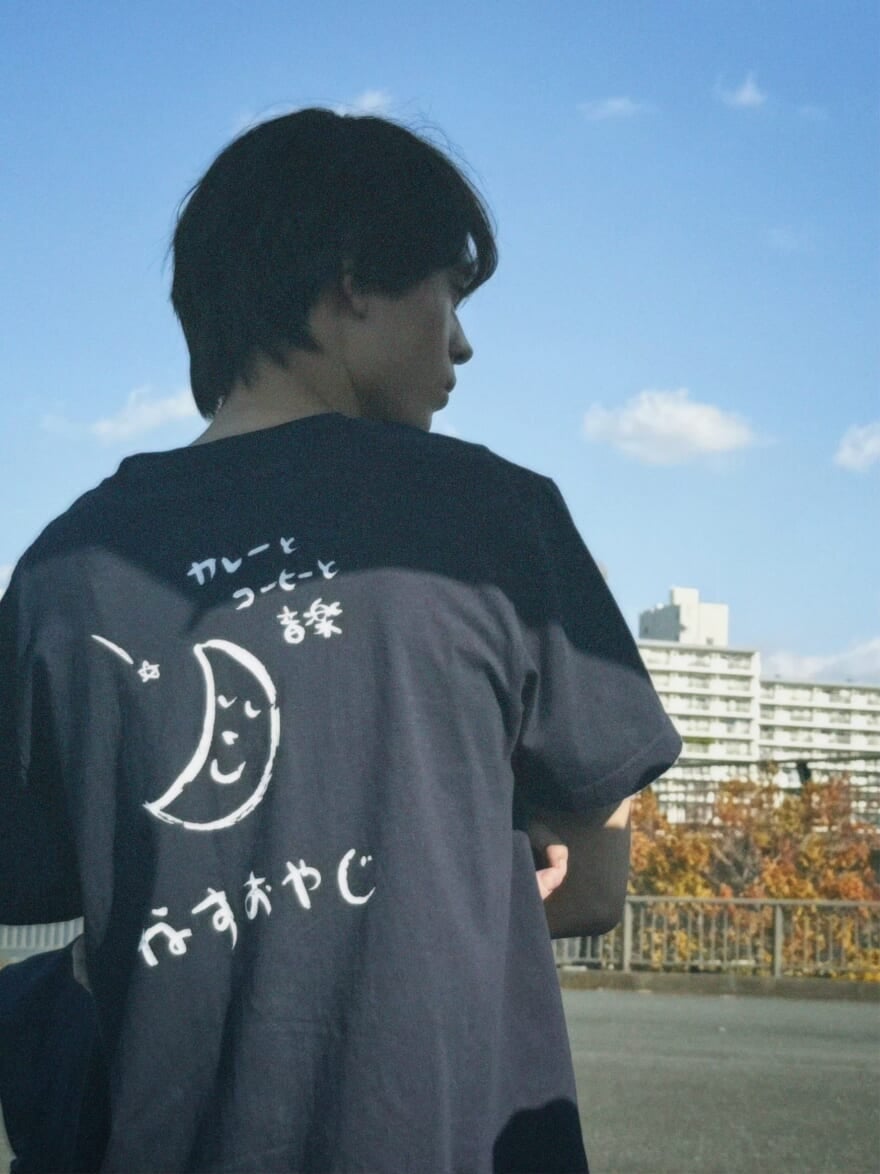 水沢林太郎の背中。「なすおやじ」と書かれた黒いTシャツを着ている